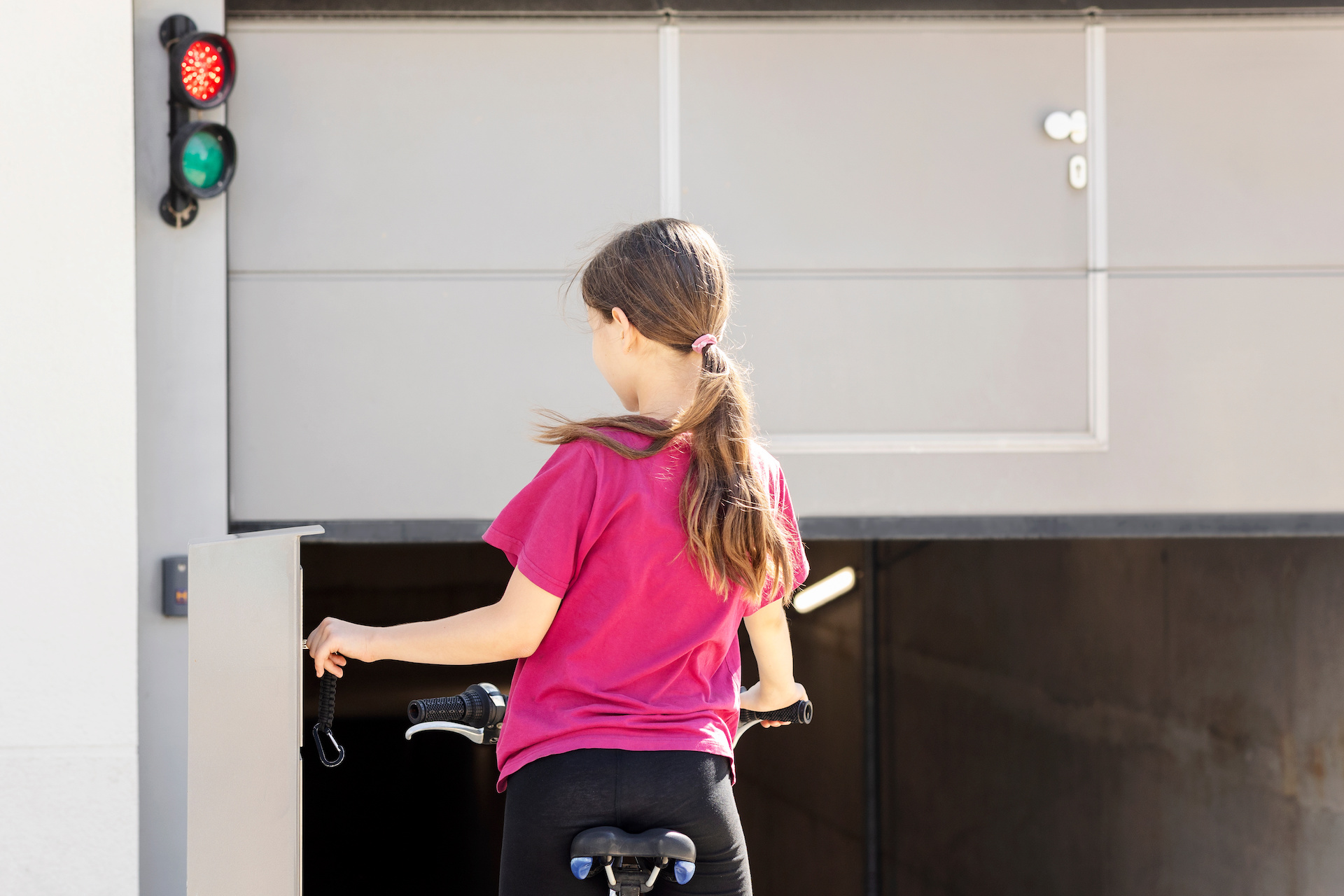 Menina de bicicleta abrindo portão da garagem